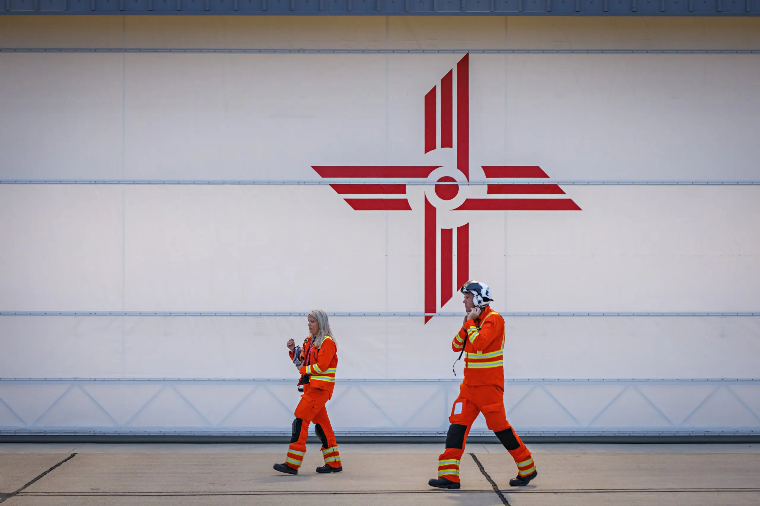 EAAA crew in orange flight suits and holding helmets walking across helipad