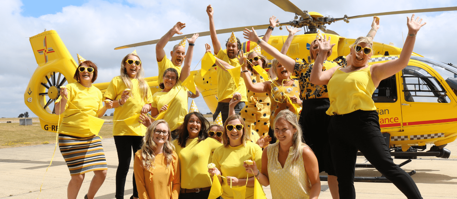 Group of people taking part in EAAA's 'Get Up and Go Yellow' and wearing yellow in front of yellow helicopter