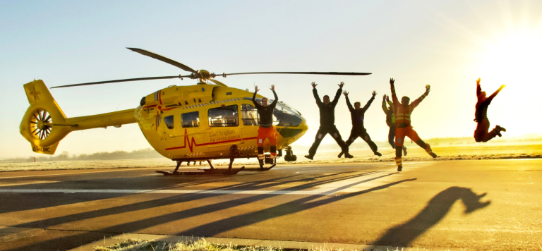 Crew jumping next to yellow, EAAA helicopter at sunset creating shadows on the ground